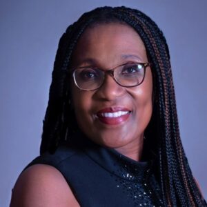 A woman with long braids wearing glasses and a black top.