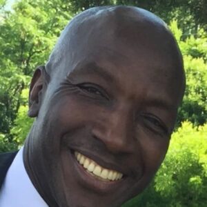 A man smiling for the camera in front of trees.