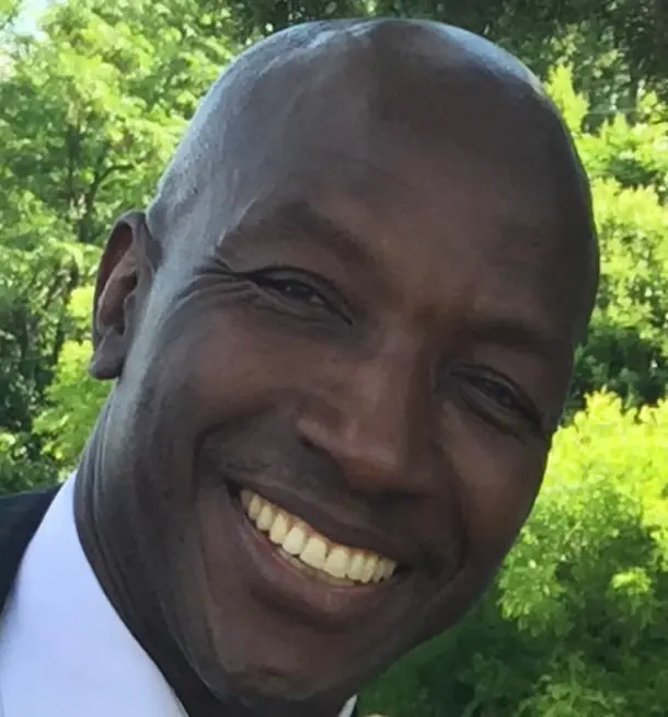 A man smiling for the camera in front of trees.