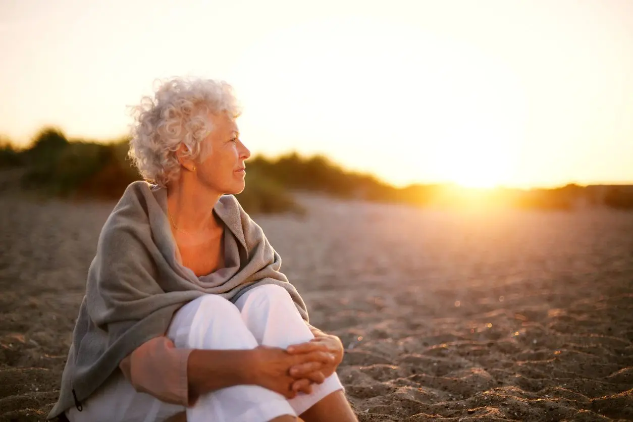 A woman sitting on the beach looking out at the sunset.