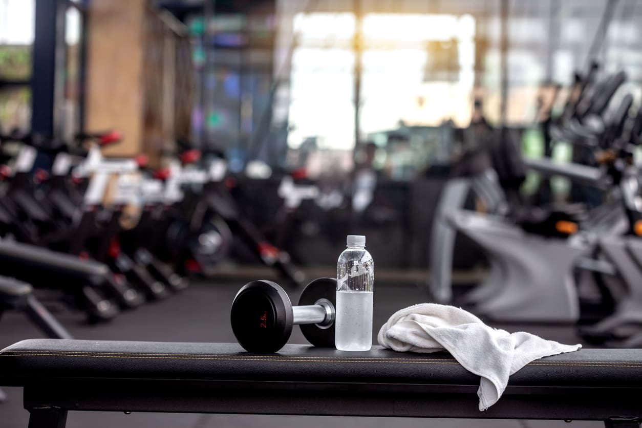 Dumbbell, water bottle, towel on gym bench.