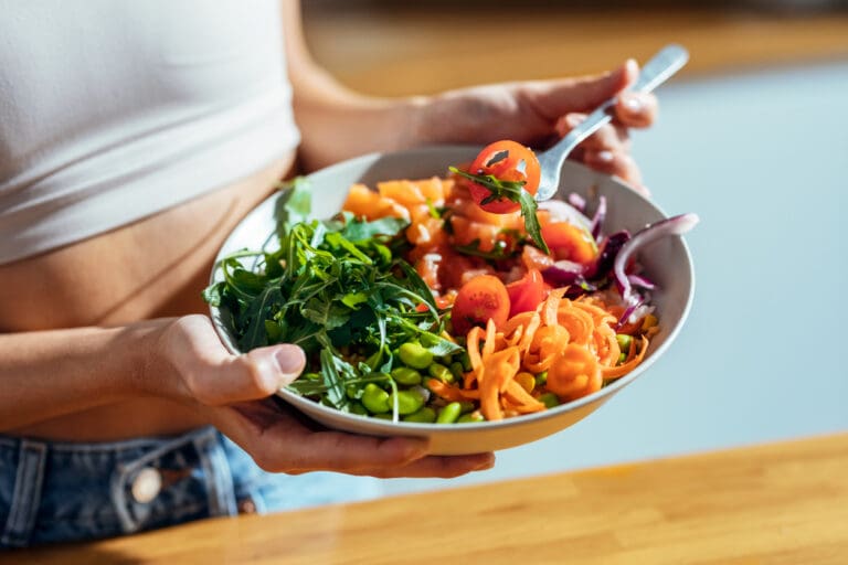 Person holding a colorful vegetable salad bowl.